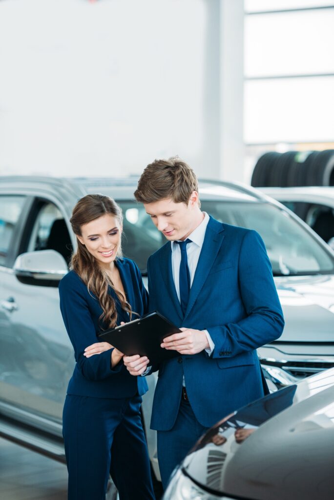 Female and male Sales managers of a car showroom standing and looking at clipboard